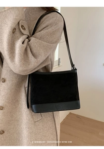 Side view of model wearing black suede tote bag with leather strap and metal buckle detail