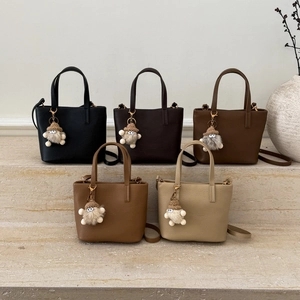 Minimalist leather bucket bags in five colors with fuzzy monster charms on stone steps