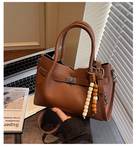 Detailed view of a brown leather handbag with litchi grain and a stylish beaded charm