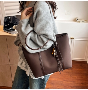 Detail of dark brown tote bag featuring matte lychee leather and bead tassel charm