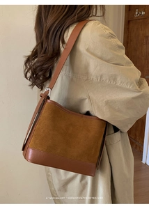 Close-up of retro brown suede shoulder bag worn with a khaki coat in a minimalist setting