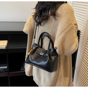 Detail of black pebbled leather handbag with silver twist lock and colorful wooden beads