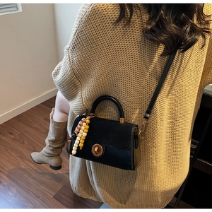 Detail of black crossbody bag with gold buckle and beaded charm worn by a model