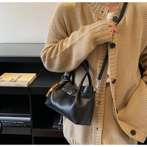 Detail of black pebbled leather crossbody bag with ethnic wooden bead charm and metal lock