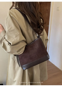 Detail of dark brown suede shoulder bag worn with a khaki coat in a minimal indoor setting