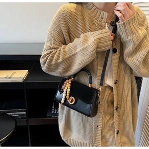 Detail of a black leather crossbody bag with wooden bead charm on a beige knit cardigan