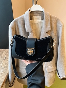 Minimalist black leather and suede shoulder bag with gold hardware on a wooden table
