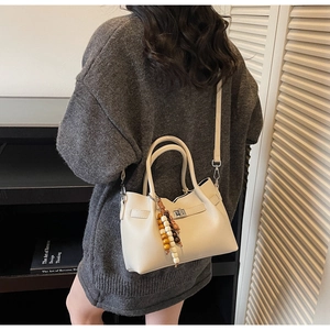 Detail of a beige textured shoulder bag featuring silver hardware and a colorful wood bead charm