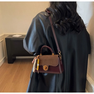 Detail of retro small crossbody bag with brown leather patchwork and bead charm