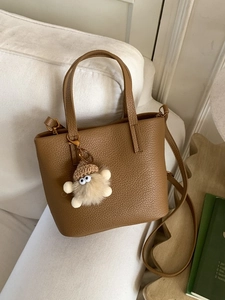Brown litchi leather tote bag with crossbody strap and cute plush charm on white sofa