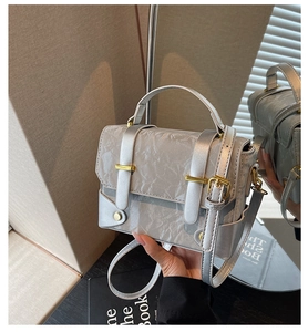 Detail of silver metallic crossbody bag with pleated texture and gold buckle accents