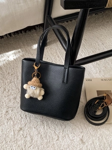 Elegant black lychee grain tote bag with gold hardware and plush bear charm on a rug