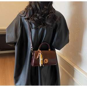 Detailed view of burgundy vintage crossbody bag with gold twist lock and beaded tassel charm
