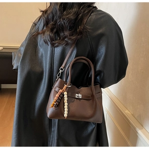 Detail of dark brown leather crossbody bag with silver twist lock and beaded charm