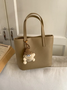 Elegant khaki textured leather tote bag with a cute monster charm on a cozy white sofa
