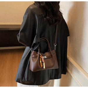 Detail of dark brown leather square crossbody bag with silver buckle and bead chain charm