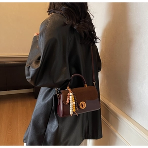 Detail of dark red leather handbag with suede flap and beaded charm on model