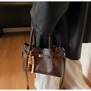 Detail of dark brown lychee leather crossbody bag featuring vintage clasp and beaded charm