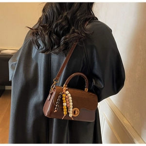 Close-up of brown patchwork leather bag with golden twist lock and bead tassel detail