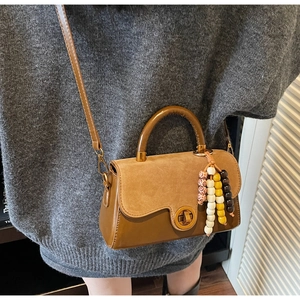 Close-up of brown suede crossbody bag featuring vintage lock and colorful wood bead charm
