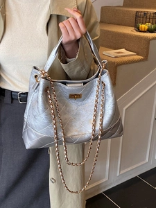 Chic silver quilted tote bag with gold chain strap shown in a stylish indoor setting
