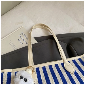 Close-up of blue and white striped tote bag featuring faux leather trim and plush charm