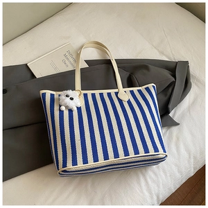 Detail of blue striped tote bag with plush monster charm and cream white handles