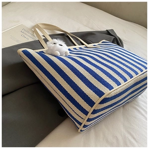 Detail of blue and white striped knit tote bag with cream leather straps and plush charm