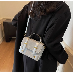 Detail of silver pleated mini shoulder bag with gold buckles on a black blazer