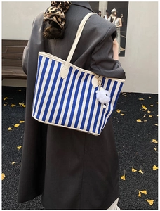 Detail of blue and white striped tote bag with plush pompom on a street background