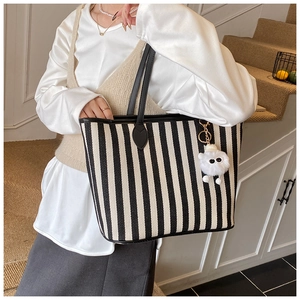 Detailed view of black and white striped tote bag with plush charm and black leather handles