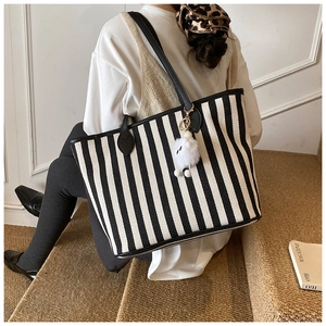 Close-up of black and white striped canvas tote bag with black leather straps and plush charm
