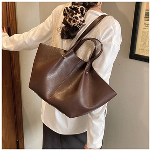 Detail view of large dark brown leather tote bag with wing shape and metal rivets