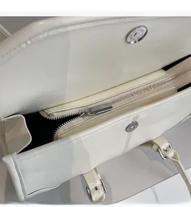 Detail of silver magnetic buckle and smooth metal zipper on white wax leather bag