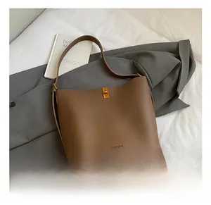 Détail du sac seau en cuir grainé marron avec boucle dorée posé sur un manteau gris
