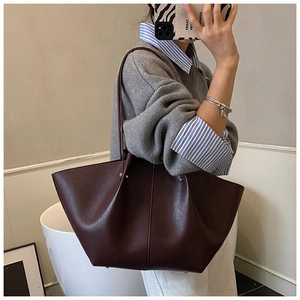 Detail of burgundy tote bag showing matte leather texture and metal corner feet