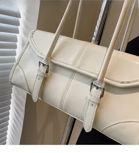 Close-up of cream leather baguette bag featuring silver buckles and fine stitching