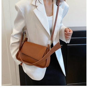 Close-up of brown textured leather shoulder bag with gold hardware on white suit model
