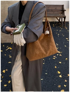 Detail of a large brown suede tote bag styled with a small green pouch on a wooden bench