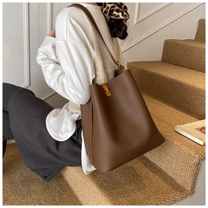 Détail du sac seau en cuir marron avec boucle dorée sur un escalier texturé