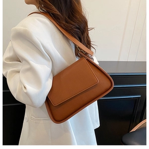 Close-up of brown litchi pattern leather shoulder bag on model wearing white suit