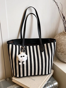Striped canvas tote bag with black leather straps and plush charm in a lifestyle setting