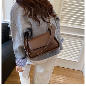 Brown textured leather crossbody bag with golden buckle shown on shoulder of a model