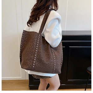 Detail of large leopard print tote bag with silver studs worn by a model in white blazer
