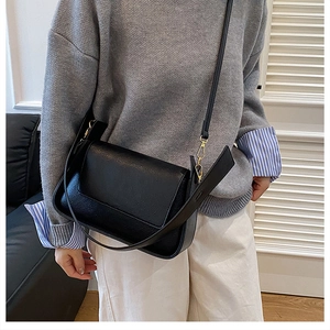 Detail of black pebbled leather crossbody bag with elegant gold hardware on model