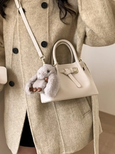 Chic beige bucket bag with plush bunny charm worn by model in elegant wool coat