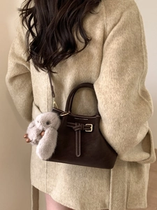 Dark brown bucket bag with contrast stitching and plush charm worn on beige coat
