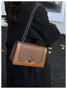 Detail of a brown chain bag with woven panel and silver hardware worn over a black coat