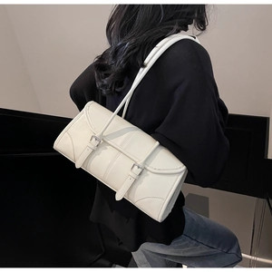 Close-up of cream white faux leather baguette bag worn over shoulder with metal buckle detail