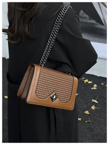 Close-up of brown textured shoulder bag with vintage metal buckle and chain strap